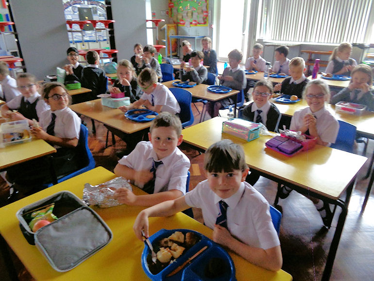 A room of children eating school dinners and packed lunches